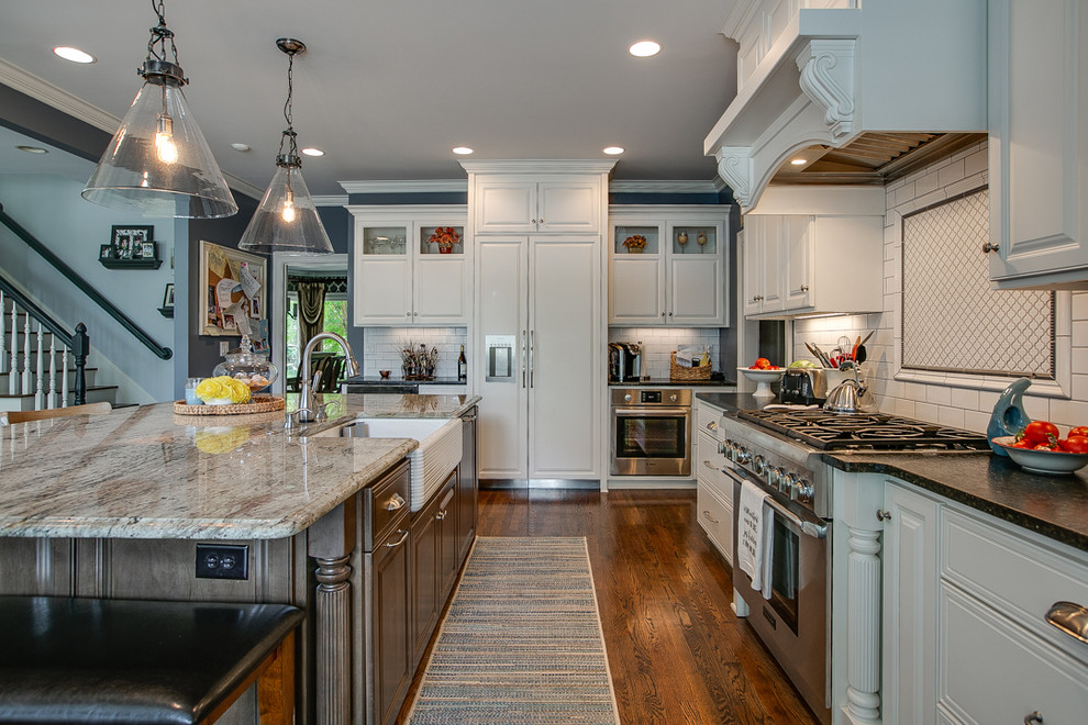 Large transitional l-shaped medium tone wood floor and brown floor open concept kitchen photo in Charlotte with a farmhouse sink, white cabinets, granite countertops, white backsplash, stainless steel appliances, an island, raised-panel cabinets, porcelain backsplash and white countertops