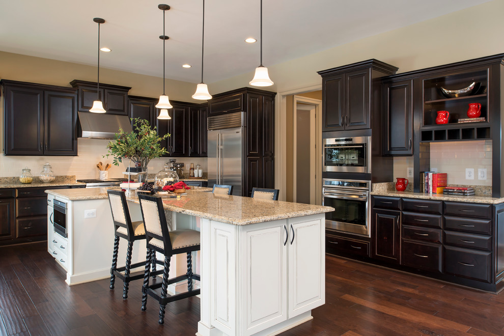 Inspiration for a traditional l-shaped kitchen in DC Metro with raised-panel cabinets, dark wood cabinets, white splashback, subway tile splashback, stainless steel appliances, dark hardwood floors, with island and brown floor.