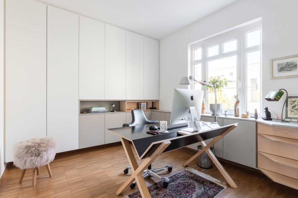 This is an example of a small contemporary study in Dusseldorf with white walls, light hardwood flooring, a freestanding desk and brown floors.
