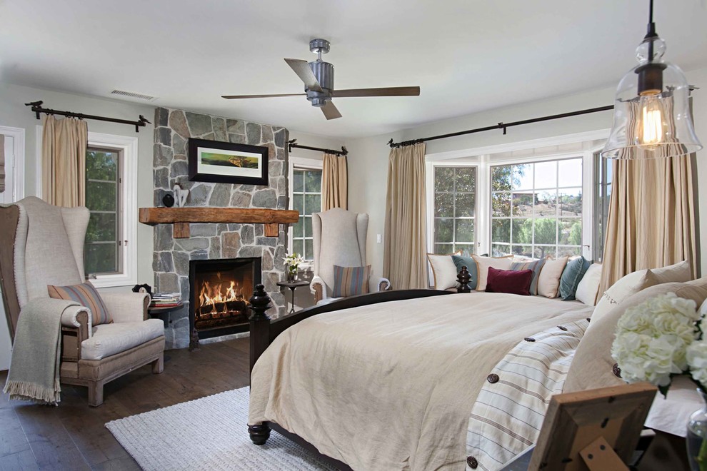 This is an example of a country bedroom in San Diego with grey walls, dark hardwood floors, a standard fireplace and a stone fireplace surround.