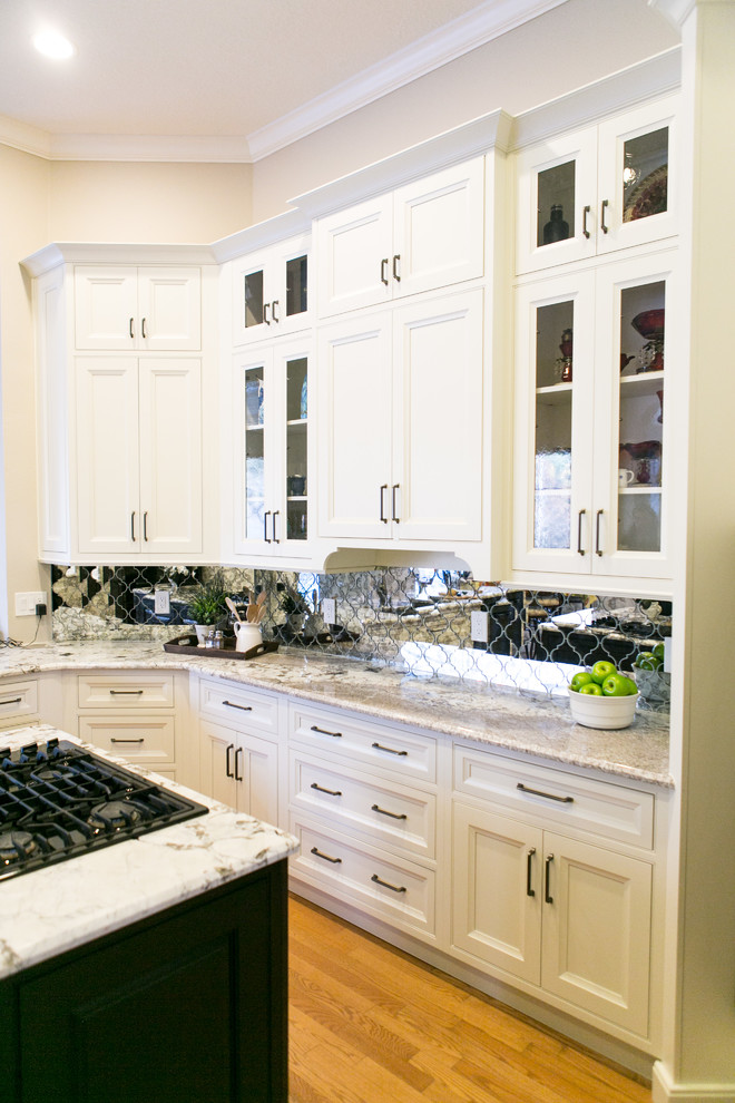 Mid-sized transitional u-shaped light wood floor and brown floor open concept kitchen photo in Orlando with an undermount sink, recessed-panel cabinets, white cabinets, granite countertops, mirror backsplash, black appliances and an island