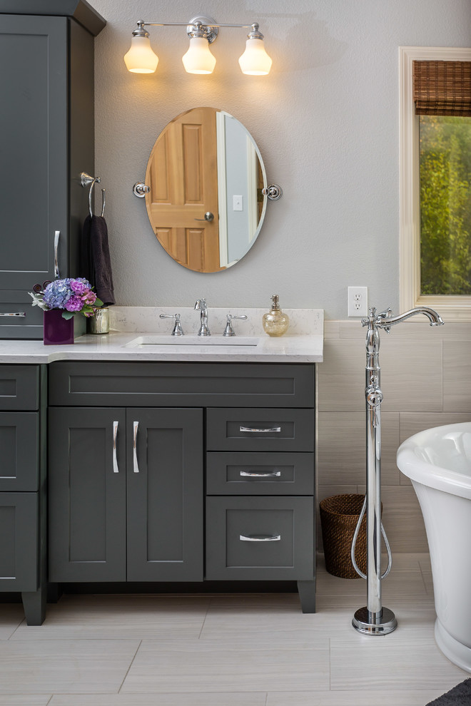 This is an example of a mid-sized transitional master bathroom in Other with an undermount sink, shaker cabinets, grey cabinets, engineered quartz benchtops, a freestanding tub, an alcove shower, a one-piece toilet, white tile, porcelain tile, grey walls and porcelain floors.