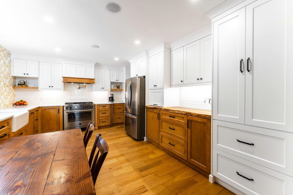 Inspiration for a mid-sized country l-shaped eat-in kitchen in Toronto with a farmhouse sink, shaker cabinets, brown cabinets, quartz benchtops, white splashback, subway tile splashback, stainless steel appliances, light hardwood floors, no island, orange floor and white benchtop.