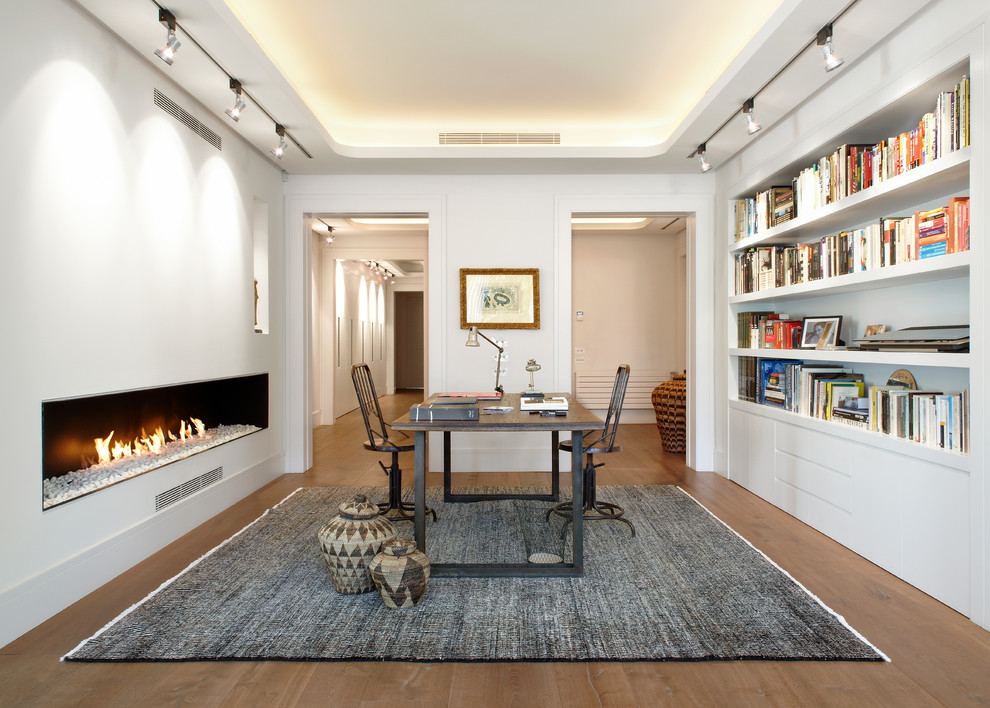 Design ideas for a mid-sized industrial study room in Barcelona with white walls, dark hardwood floors, a ribbon fireplace, a plaster fireplace surround and a freestanding desk.