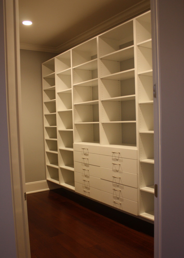 Photo of a walk-in wardrobe in New York with flat-panel cabinets, white cabinets, dark hardwood floors and brown floor.