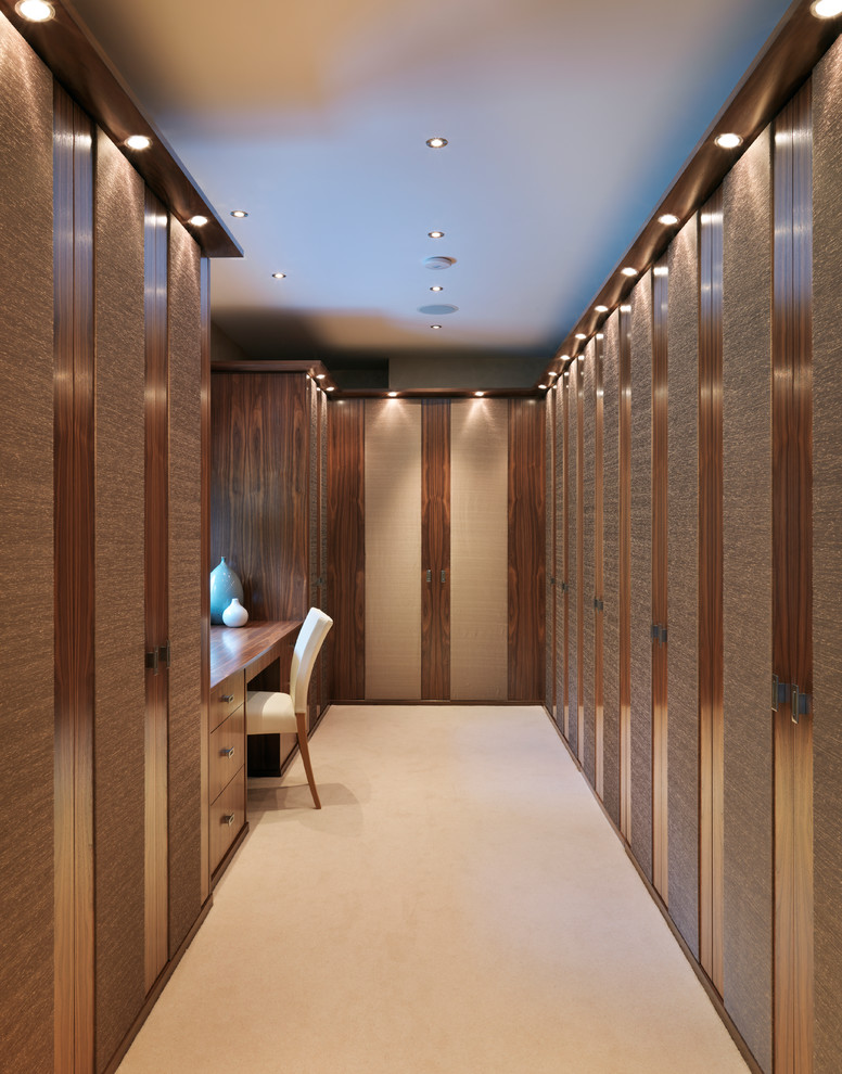 Photo of a large contemporary walk-in wardrobe in Kent with carpet, dark wood cabinets, flat-panel cabinets and beige floor.