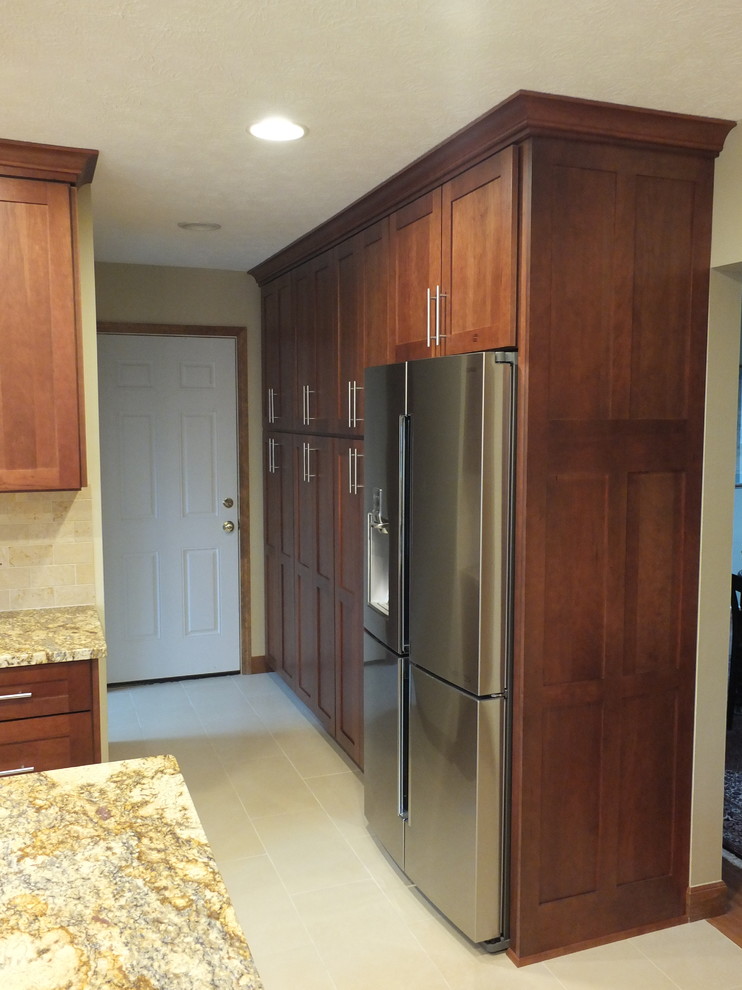 Example of a mid-sized transitional l-shaped ceramic tile eat-in kitchen design in Columbus with an undermount sink, shaker cabinets, brown cabinets, granite countertops, beige backsplash, ceramic backsplash, stainless steel appliances and an island