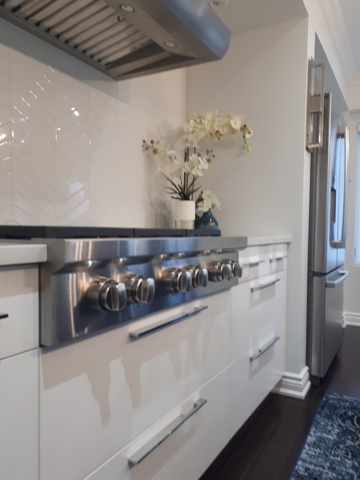 Mid-sized transitional galley medium tone wood floor and brown floor eat-in kitchen photo with a farmhouse sink, flat-panel cabinets, white cabinets, quartz countertops, white backsplash, ceramic backsplash, stainless steel appliances, an island and white countertops