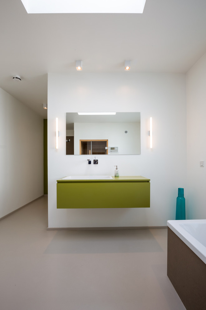 This is an example of a mid-sized contemporary master bathroom in Cologne with green cabinets, white walls, a drop-in sink, flat-panel cabinets, white tile, wood benchtops, a corner tub, concrete floors and grey floor.