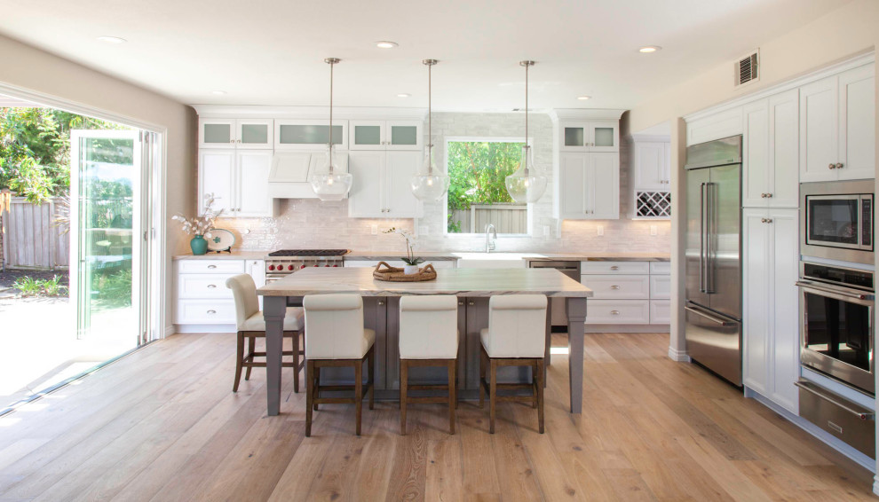 This is an example of a mid-sized beach style galley eat-in kitchen in San Diego with an undermount sink, shaker cabinets, white cabinets, quartzite benchtops, white splashback, glass tile splashback, stainless steel appliances, laminate floors, with island, brown floor and multi-coloured benchtop.