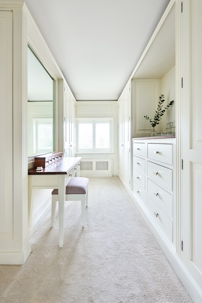 This is an example of a traditional women's dressing room in Wiltshire with white cabinets, carpet and beige floor.