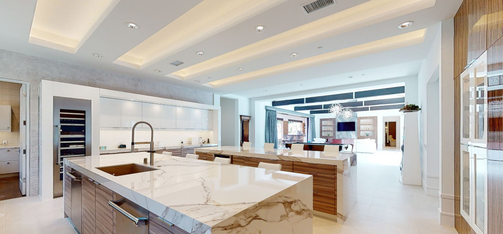 Photo of an expansive modern u-shaped kitchen in Orange County with a single-bowl sink, flat-panel cabinets, engineered stone countertops, white splashback, stone slab splashback, stainless steel appliances, porcelain flooring, multiple islands, beige floors, white worktops and a drop ceiling.