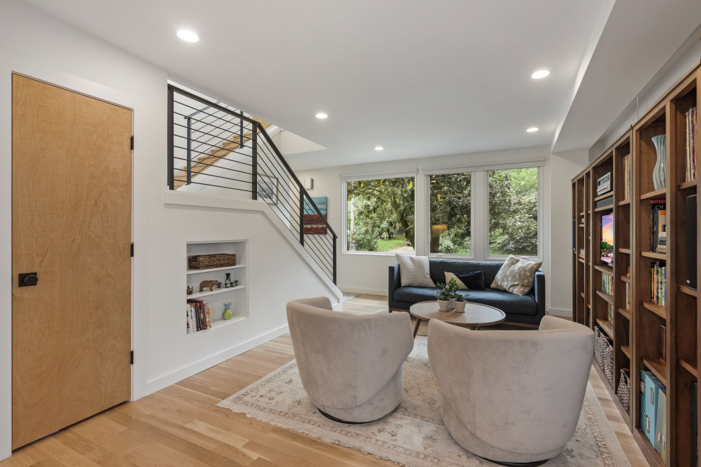 This is an example of a mid-sized modern open concept living room in DC Metro with white walls, light hardwood floors and brown floor.