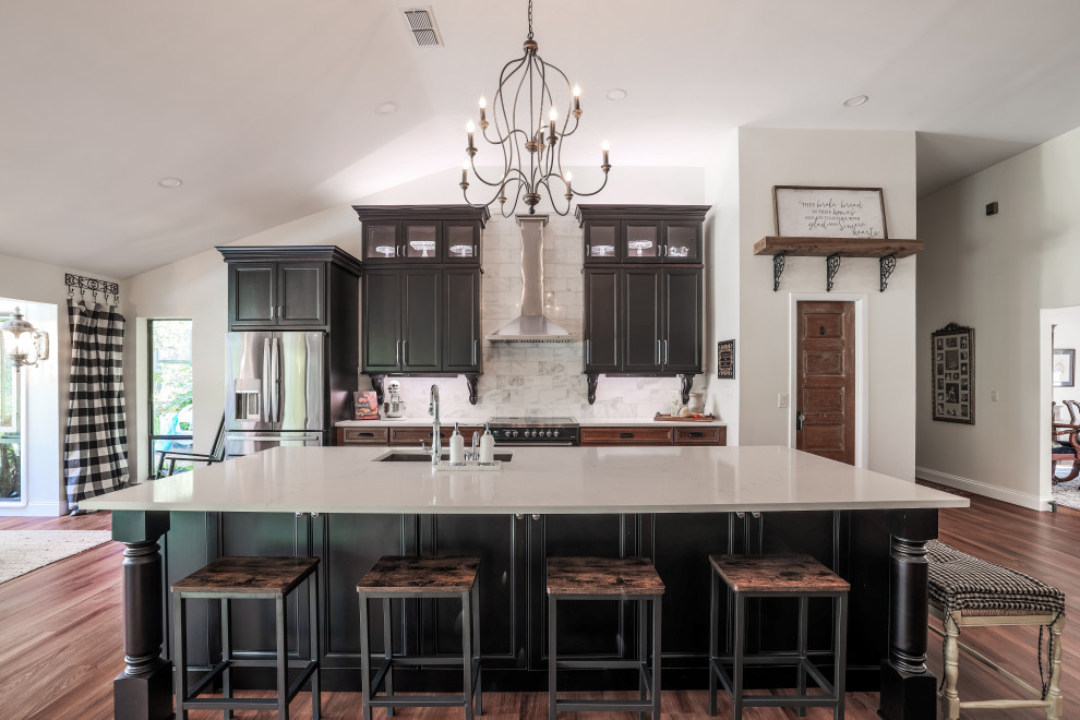 Photo of a large galley kitchen/diner in Orlando with a single-bowl sink, recessed-panel cabinets, black cabinets, engineered stone countertops, white splashback, marble splashback, stainless steel appliances, laminate floors, an island, brown floors, white worktops and a vaulted ceiling.