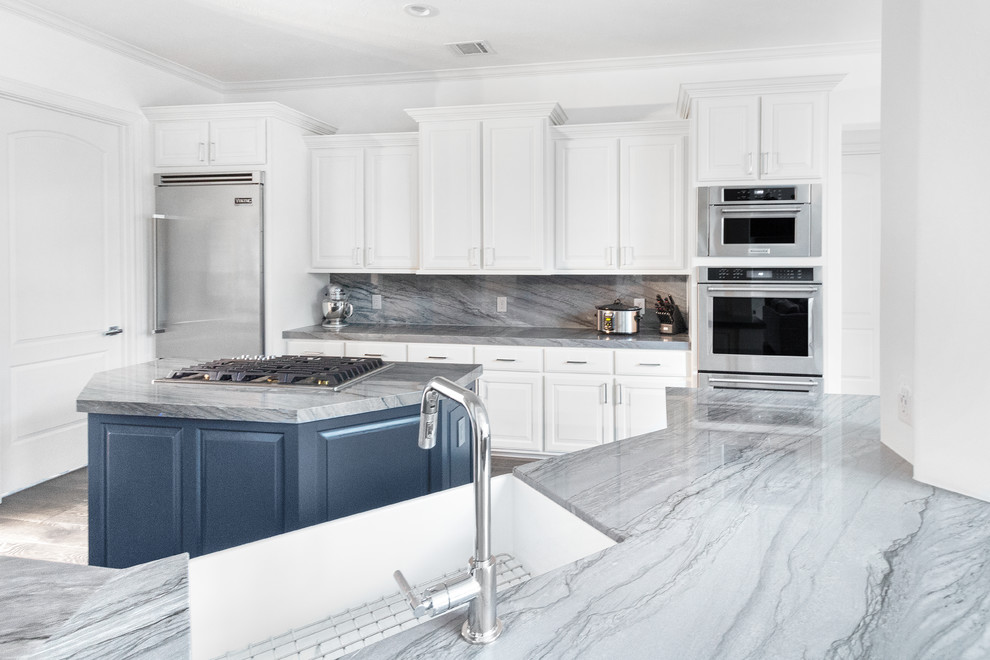 Eat-in kitchen - mid-sized transitional galley medium tone wood floor and gray floor eat-in kitchen idea in Houston with a farmhouse sink, raised-panel cabinets, blue cabinets, quartzite countertops, gray backsplash, stone slab backsplash, stainless steel appliances, an island and gray countertops
