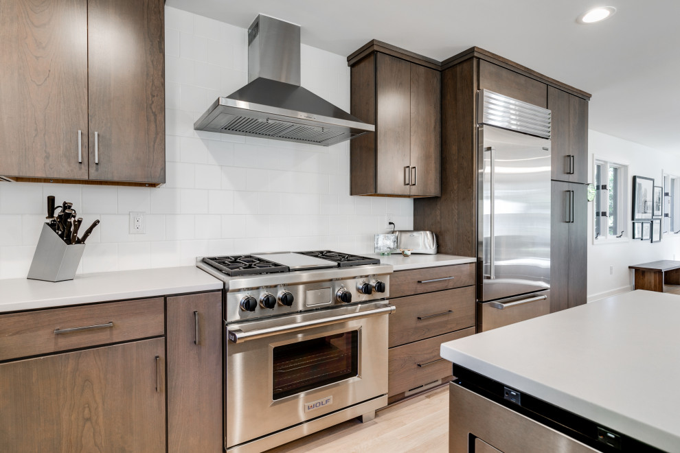Mid-sized modern u-shaped open plan kitchen in Richmond with an undermount sink, flat-panel cabinets, brown cabinets, white splashback, ceramic splashback, stainless steel appliances, light hardwood floors, with island and white benchtop.