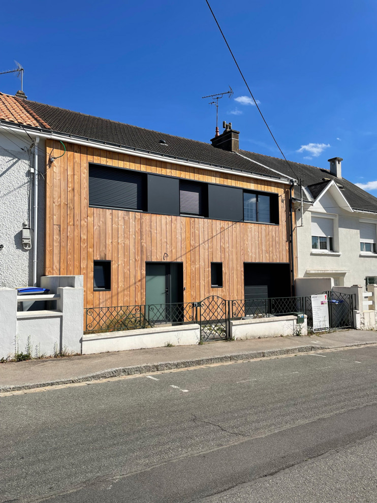 Photo of a mid-sized contemporary two-storey grey townhouse exterior in Nantes with wood siding, a gable roof, a tile roof, a brown roof and board and batten siding.