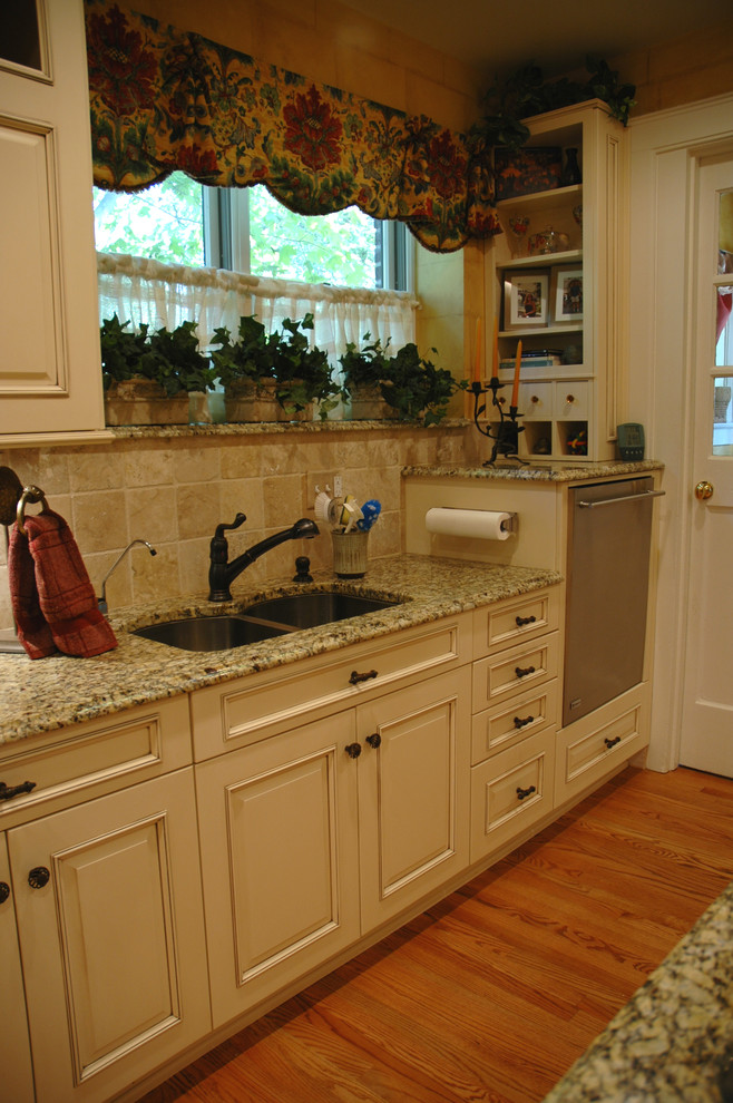 This is an example of a mediterranean l-shaped separate kitchen in Indianapolis with an undermount sink, raised-panel cabinets, beige cabinets, granite benchtops, stainless steel appliances, light hardwood floors and with island.