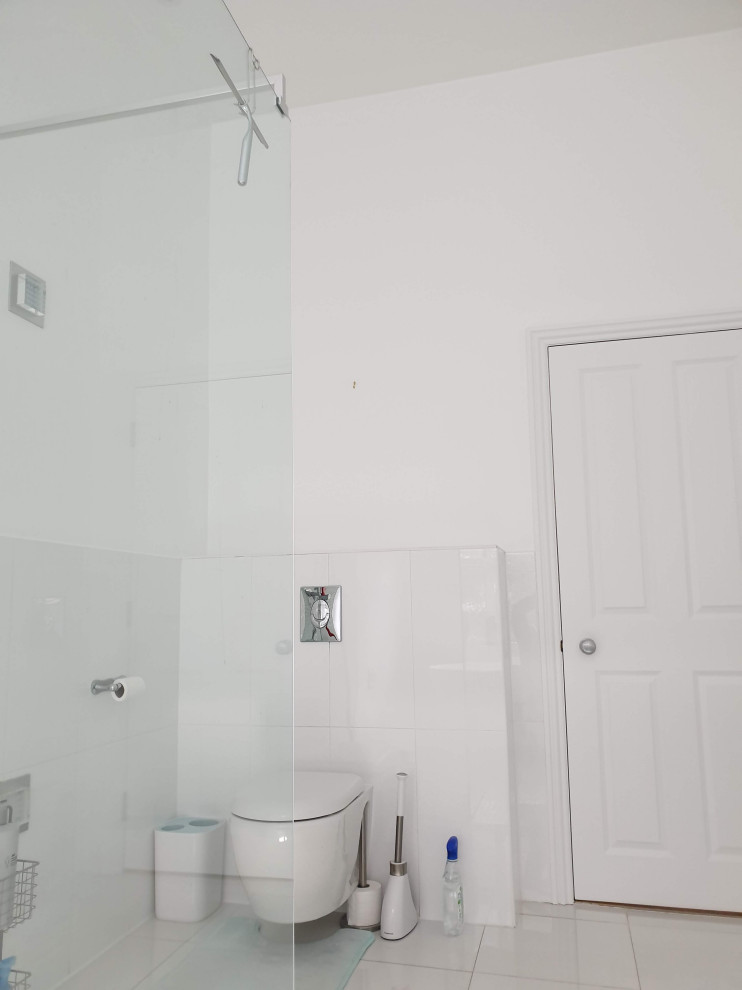 Large modern kids bathroom in London with flat-panel cabinets, white cabinets, a freestanding tub, an open shower, a wall-mount toilet, white tile, porcelain tile, white walls, pebble tile floors, a drop-in sink, marble benchtops, white floor, an open shower, white benchtops, a single vanity, a built-in vanity and recessed.