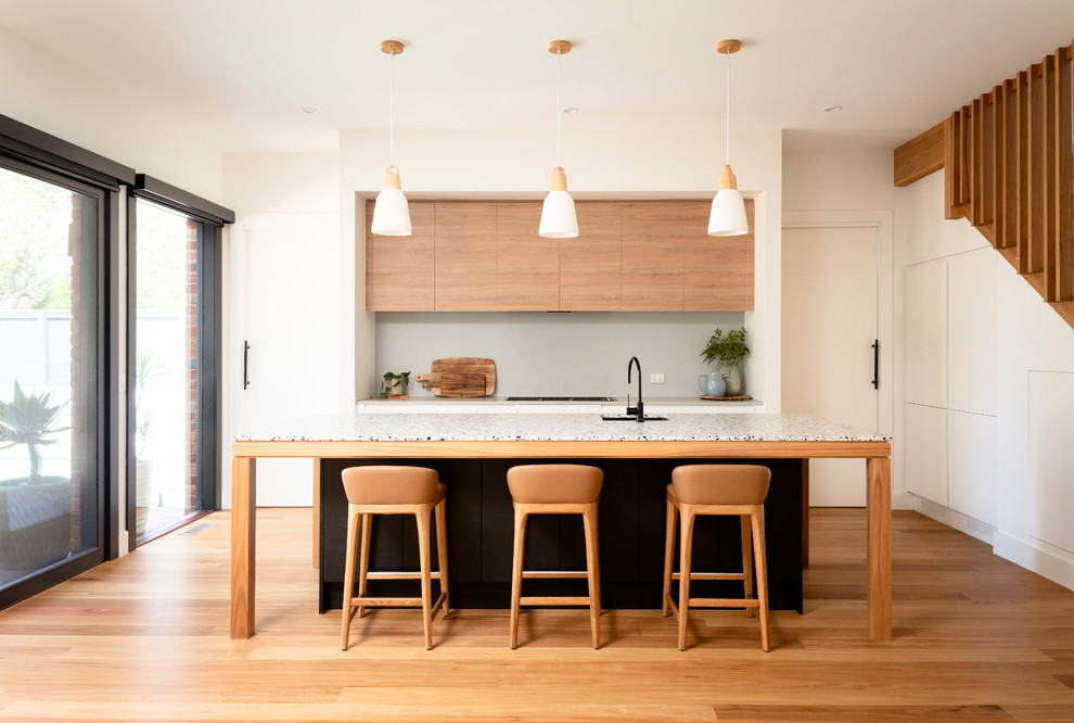 This is an example of a contemporary galley kitchen in Melbourne with an undermount sink, flat-panel cabinets, medium wood cabinets, panelled appliances, medium hardwood floors, with island, brown floor and white benchtop.