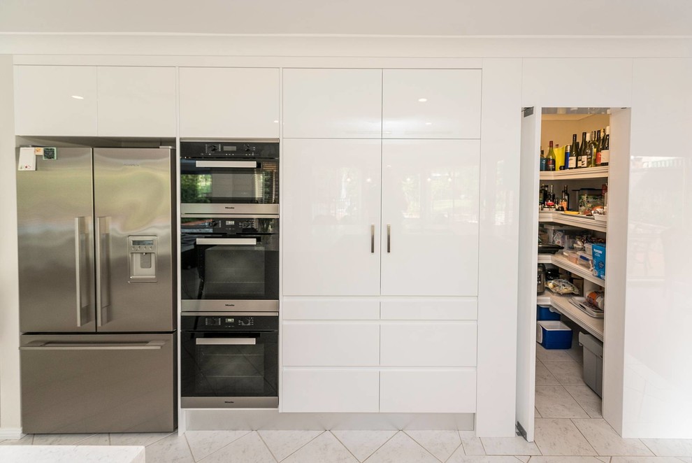 Large contemporary u-shaped open plan kitchen in Sydney with a drop-in sink, flat-panel cabinets, white cabinets, quartz benchtops, marble splashback, stainless steel appliances, ceramic floors, with island, grey splashback and grey benchtop.
