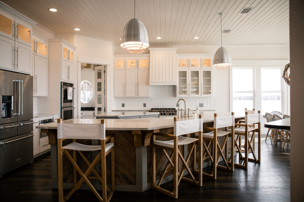 Design ideas for a large beach style l-shaped open plan kitchen in Dallas with shaker cabinets, white cabinets, multiple islands, marble benchtops, white splashback, a farmhouse sink, ceramic splashback, stainless steel appliances, dark hardwood floors and brown floor.