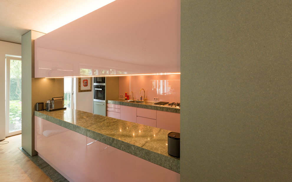 This is an example of a mid-sized midcentury galley open plan kitchen in Other with a single-bowl sink, flat-panel cabinets, granite benchtops, pink splashback, glass sheet splashback, with island and grey floor.