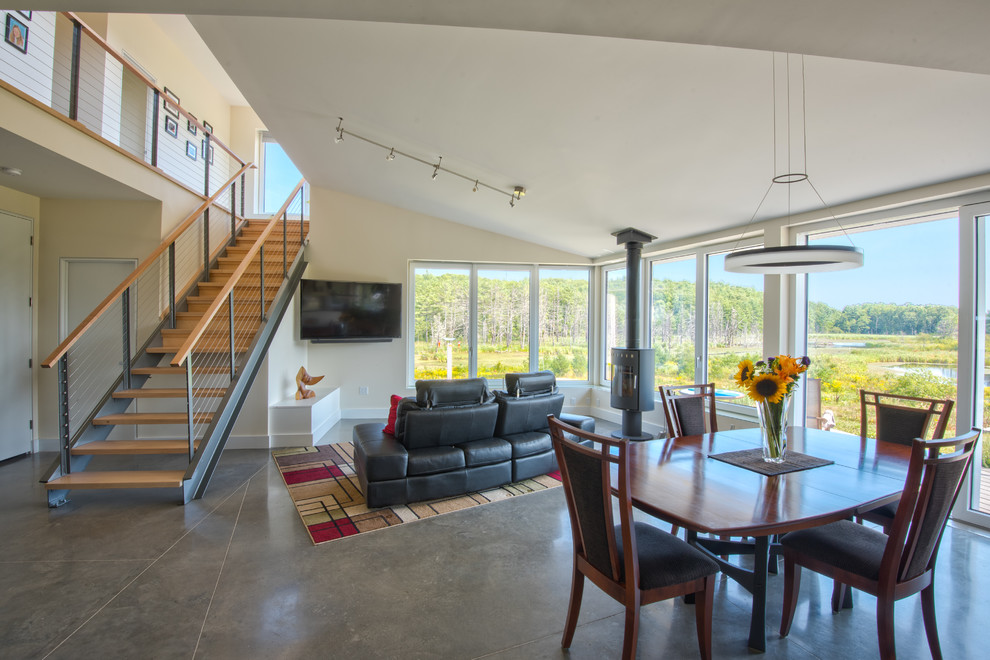 This is an example of a mid-sized contemporary open plan dining in Portland Maine with beige walls, concrete floors, a wood stove and grey floor.