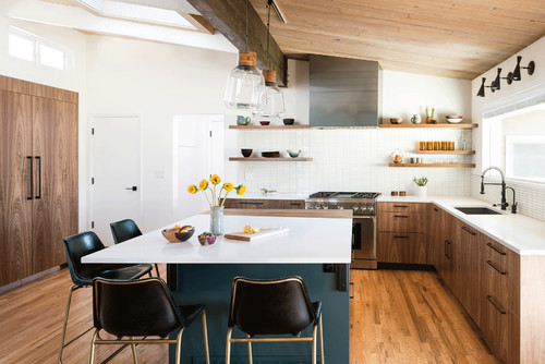 Warm modern kitchen with flat-panel walnut RTA cabinets, white quartz counters, teal peninsula, open wood shelves, stainless hood, and a sloped wood ceiling with beams.