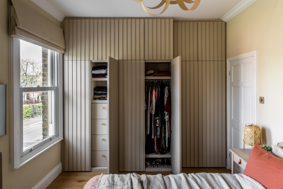 Design ideas for a small gender-neutral storage and wardrobe in London with raised-panel cabinets, beige cabinets and medium hardwood floors.