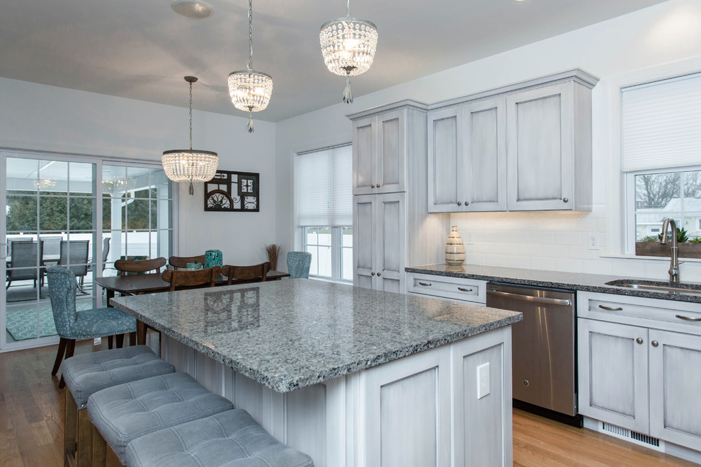Mid-sized traditional l-shaped eat-in kitchen in Boston with an undermount sink, recessed-panel cabinets, distressed cabinets, granite benchtops, white splashback, ceramic splashback, stainless steel appliances, medium hardwood floors and with island.