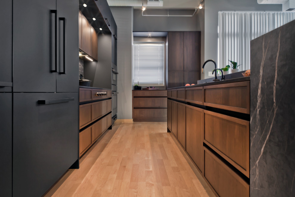 Design ideas for a mid-sized contemporary l-shaped eat-in kitchen in Minneapolis with an undermount sink, recessed-panel cabinets, quartz benchtops, metallic splashback, porcelain splashback, panelled appliances, light hardwood floors, with island, brown floor, black benchtop and medium wood cabinets.