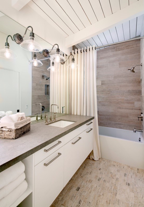 This is an example of a mid-sized beach style bathroom in Santa Barbara with flat-panel cabinets, white cabinets, an alcove tub, a shower/bathtub combo, white walls, limestone floors, an undermount sink, brown tile and concrete benchtops.