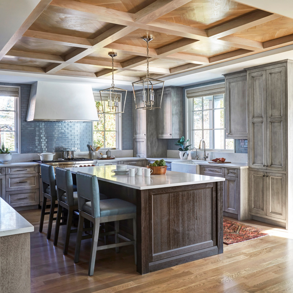 Design ideas for a large traditional u-shaped kitchen in Chicago with a farmhouse sink, recessed-panel cabinets, grey cabinets, blue splashback, subway tile splashback, stainless steel appliances, medium hardwood floors, with island, white benchtop, coffered, wood and brown floor.