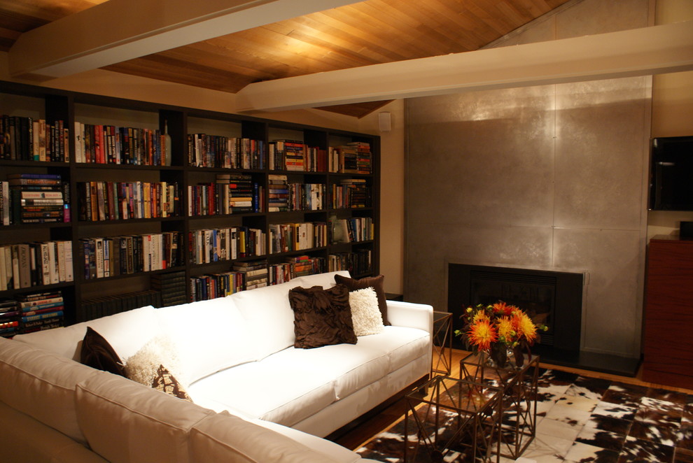 This is an example of a modern living room in Seattle with a library, a standard fireplace and a metal fireplace surround.