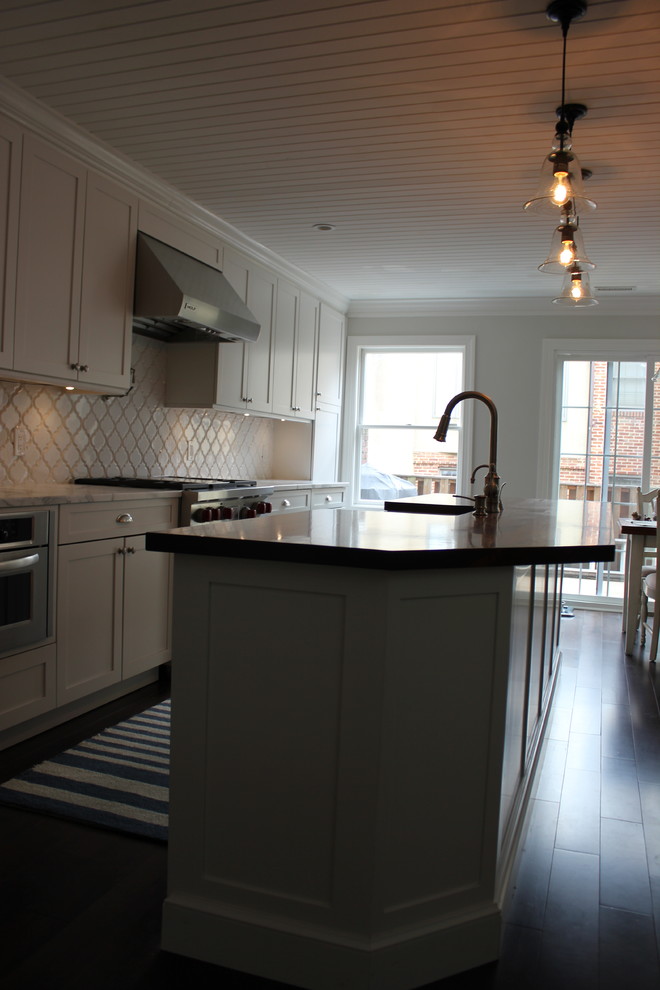 Inspiration for a large transitional galley dark wood floor eat-in kitchen remodel in Baltimore with a farmhouse sink, shaker cabinets, white cabinets, wood countertops, white backsplash, ceramic backsplash, stainless steel appliances and an island