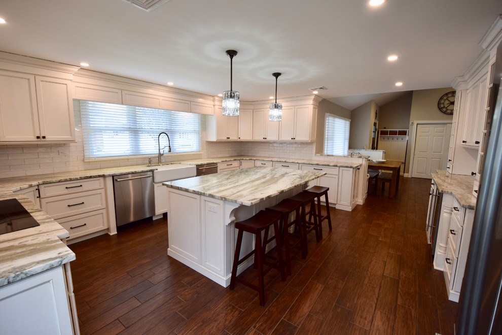 Example of a large transitional u-shaped dark wood floor and brown floor enclosed kitchen design with a farmhouse sink, beaded inset cabinets, white cabinets, granite countertops, beige backsplash, ceramic backsplash, stainless steel appliances, an island and multicolored countertops