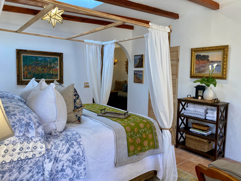 サンディエゴにある中くらいな地中海スタイルのおしゃれな客用寝室 (白い壁、磁器タイルの床、コーナー設置型暖炉、漆喰の暖炉まわり、オレンジの床、表し梁、間仕切りカーテン、白い天井)