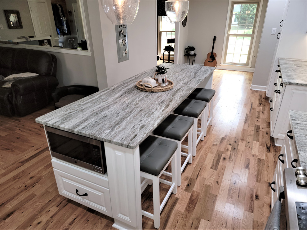 Large country l-shaped eat-in kitchen in Richmond with an undermount sink, raised-panel cabinets, white cabinets, quartzite benchtops, beige splashback, porcelain splashback, stainless steel appliances, medium hardwood floors, with island, brown floor, grey benchtop and timber.