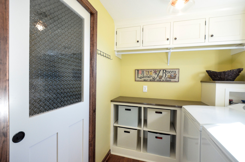 This is an example of a mid-sized country l-shaped dedicated laundry room in Kansas City with shaker cabinets, white cabinets, quartz benchtops, yellow walls, dark hardwood floors and a side-by-side washer and dryer.
