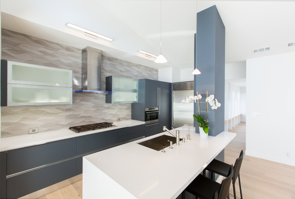 Inspiration for a mid-sized contemporary u-shaped open plan kitchen in San Francisco with an undermount sink, flat-panel cabinets, blue cabinets, grey splashback, ceramic splashback, stainless steel appliances, light hardwood floors, with island and quartz benchtops.