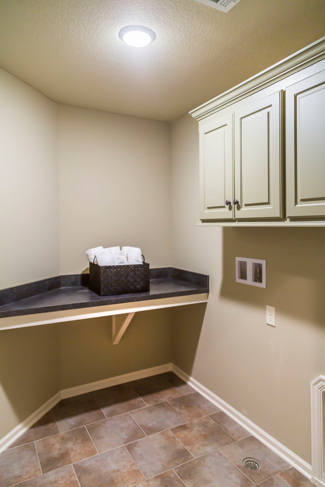 Photo of a mid-sized eclectic single-wall laundry cupboard in Kansas City with louvered cabinets, beige cabinets, solid surface benchtops, beige walls, ceramic floors, a side-by-side washer and dryer, multi-coloured floor and black benchtop.