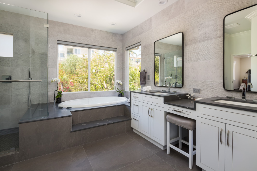 Large transitional master bathroom in Los Angeles with grey cabinets, a drop-in tub, a corner shower, a one-piece toilet, gray tile, porcelain tile, white walls, porcelain floors, an undermount sink, engineered quartz benchtops, black floor, a hinged shower door, black benchtops, a shower seat, a double vanity, a built-in vanity and flat-panel cabinets.
