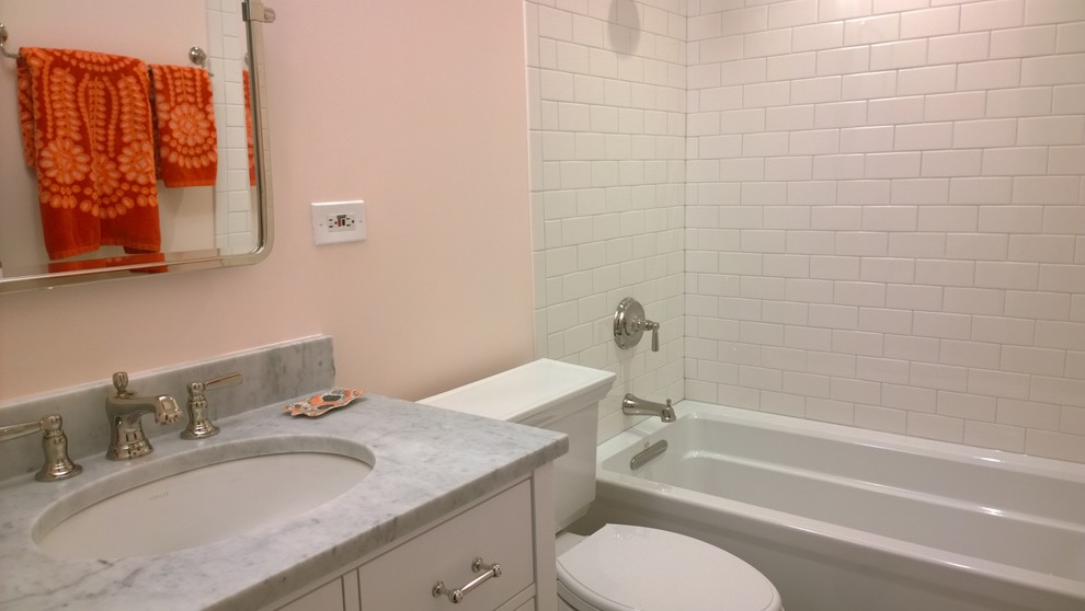 Photo of a small traditional bathroom in Chicago with an undermount sink, furniture-like cabinets, white cabinets, quartzite benchtops, an alcove tub, a shower/bathtub combo, a two-piece toilet, white tile, ceramic tile, pink walls and porcelain floors.
