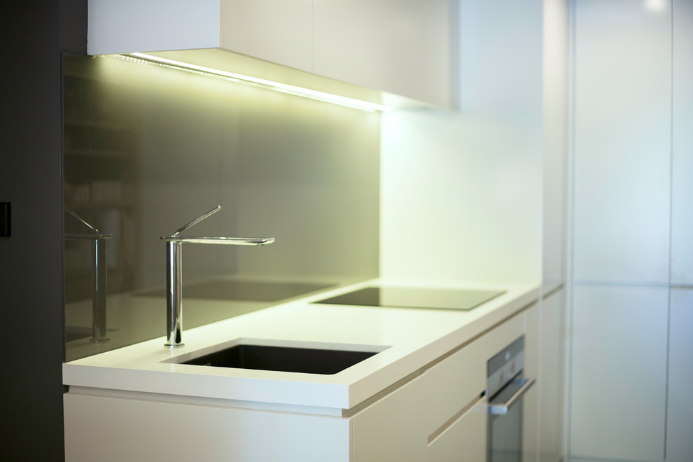 This is an example of a small contemporary l-shaped open plan kitchen in Sydney with an undermount sink, white cabinets, quartz benchtops, grey splashback, glass sheet splashback, stainless steel appliances and porcelain floors.