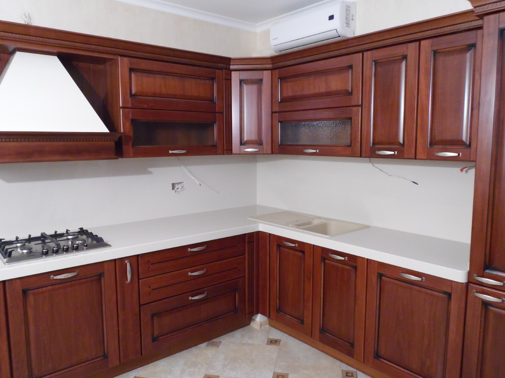 Photo of a large traditional l-shaped separate kitchen in Other with a drop-in sink, raised-panel cabinets, medium wood cabinets, solid surface benchtops, white splashback, stone slab splashback, stainless steel appliances, ceramic floors, no island, beige floor and white benchtop.