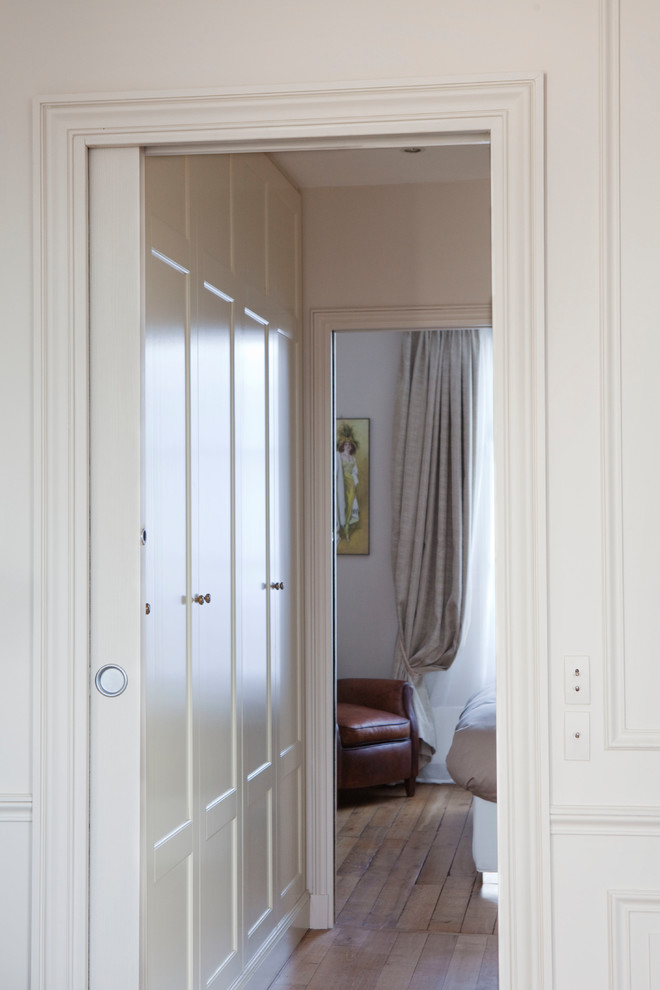 This is an example of a transitional gender-neutral dressing room in Paris with beaded inset cabinets, beige cabinets, light hardwood floors and brown floor.