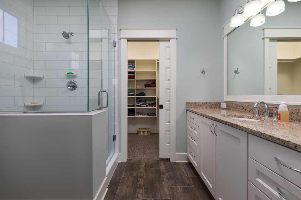 Mid-sized traditional bathroom in Grand Rapids with recessed-panel cabinets, white cabinets, an alcove shower, a one-piece toilet, white tile, subway tile, an undermount sink, granite benchtops, brown floor, a hinged shower door and beige benchtops.