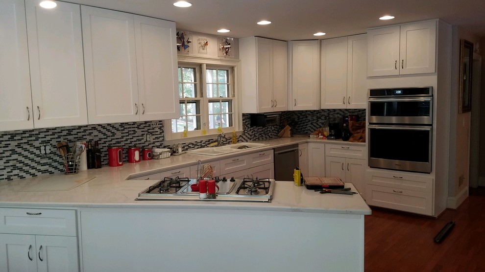 Kitchen - mid-sized transitional u-shaped medium tone wood floor and brown floor kitchen idea in Atlanta with a drop-in sink, shaker cabinets, white cabinets, solid surface countertops, multicolored backsplash, stone tile backsplash, stainless steel appliances, a peninsula and white countertops