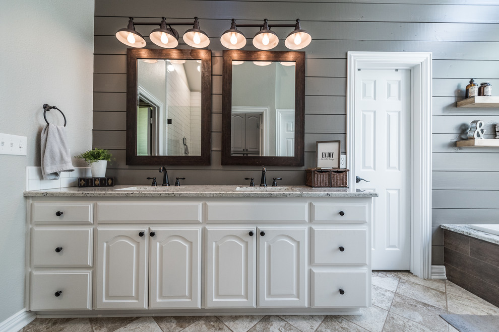 Inspiration for a mid-sized country master bathroom in Dallas with raised-panel cabinets, white cabinets, a drop-in tub, an alcove shower, gray tile, ceramic tile, grey walls, travertine floors, an undermount sink, granite benchtops, beige floor and a hinged shower door.